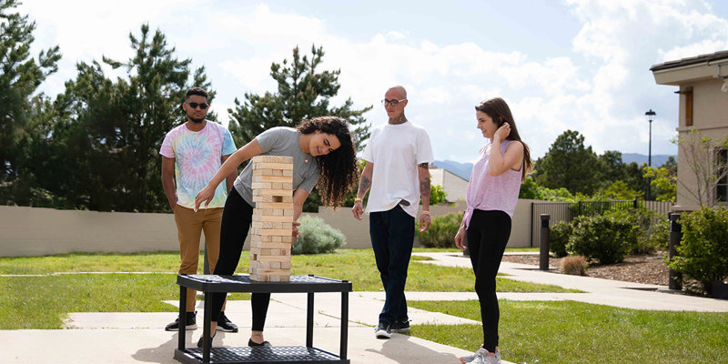 A group of young adults enjoying an outdoor game of Jenga on a sunny day, surrounded by greenery, fostering a fun and social environment.