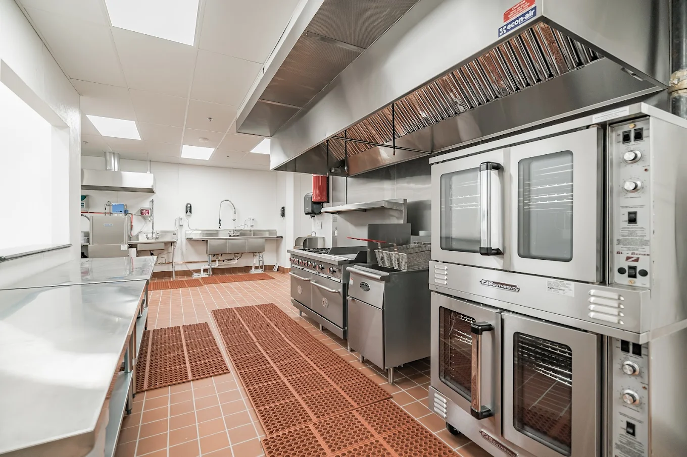 Commercial kitchen with ovens, prep tables, and ventilation