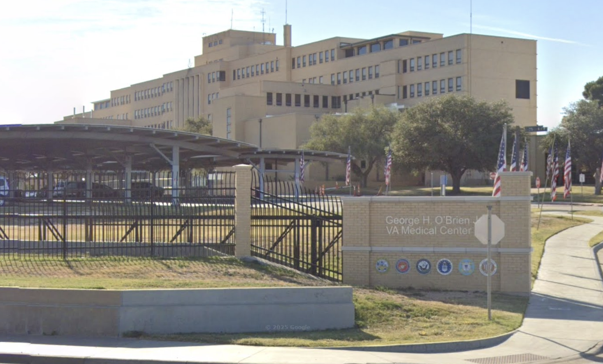 Large beige VA medical center with entrance sign and American flags