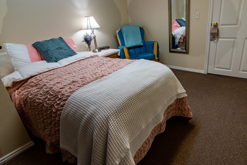 Bed with soft pink bedding and a cozy blue chair