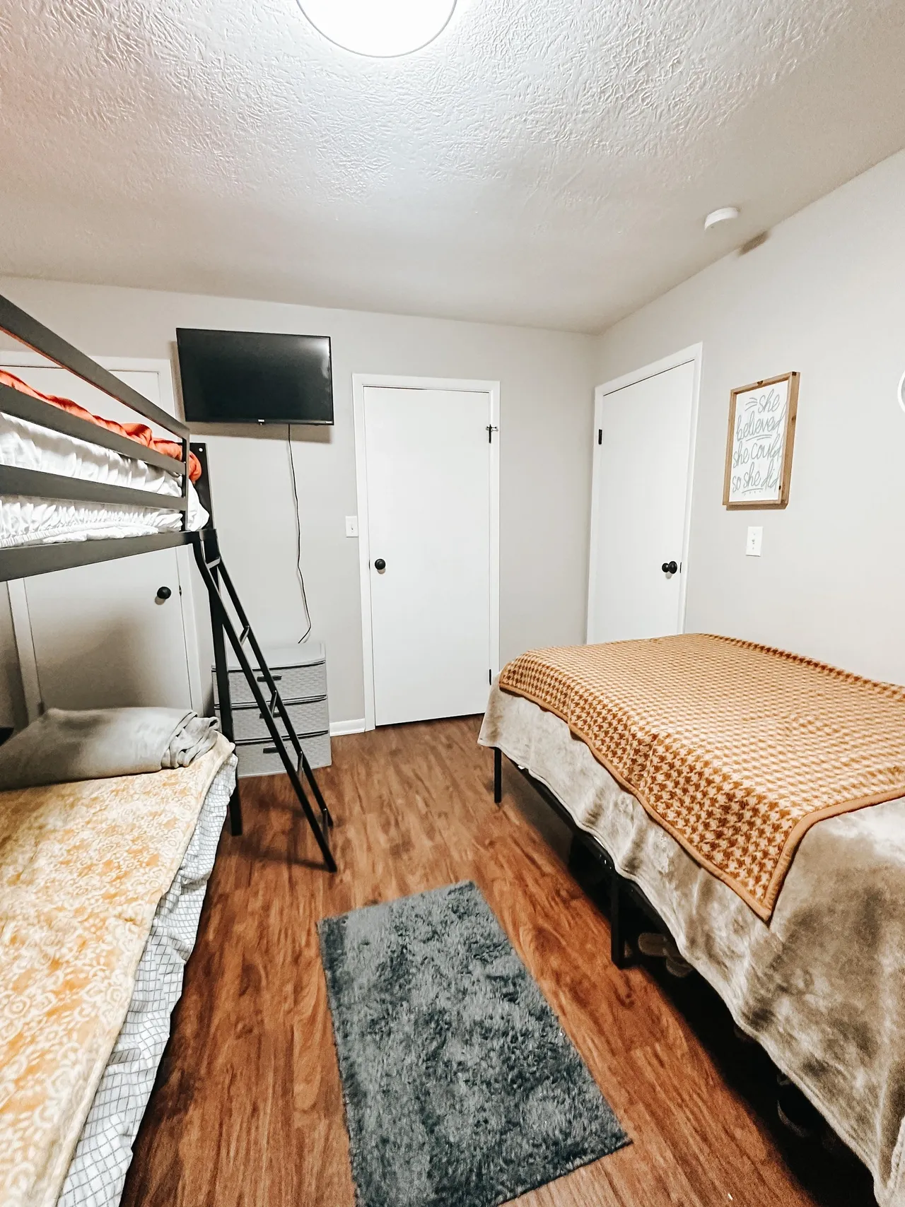 Bedroom with bunk bed and twin bed, hardwood floors, and wall-mounted TV