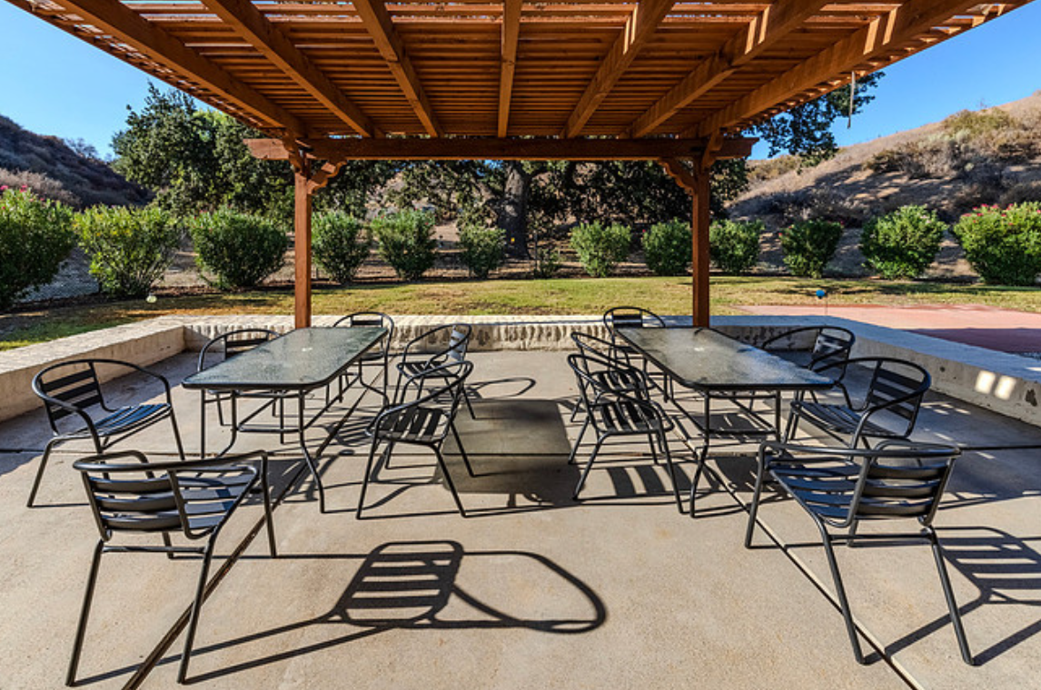 Patio with tables and chairs under wooden pergola.