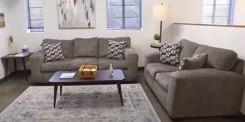 Cozy sitting area with comfortable gray sofas, patterned throw pillows, a coffee table, and soft lighting, creating a warm and inviting atmosphere.