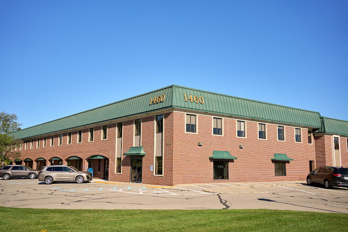 Welcoming entrance to a brick building, surrounded by a manicured lawn with visible parking.
