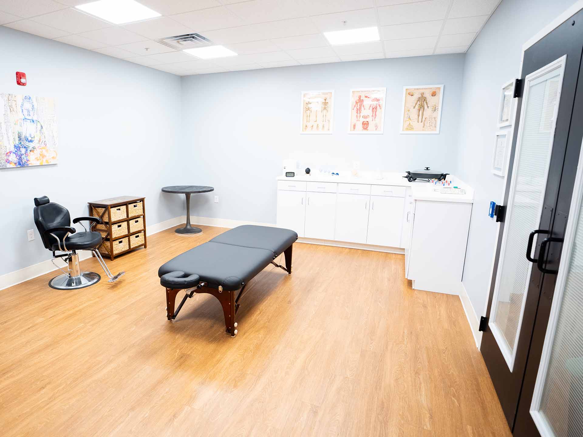 A medical room with a massage table, chair, and cabinets