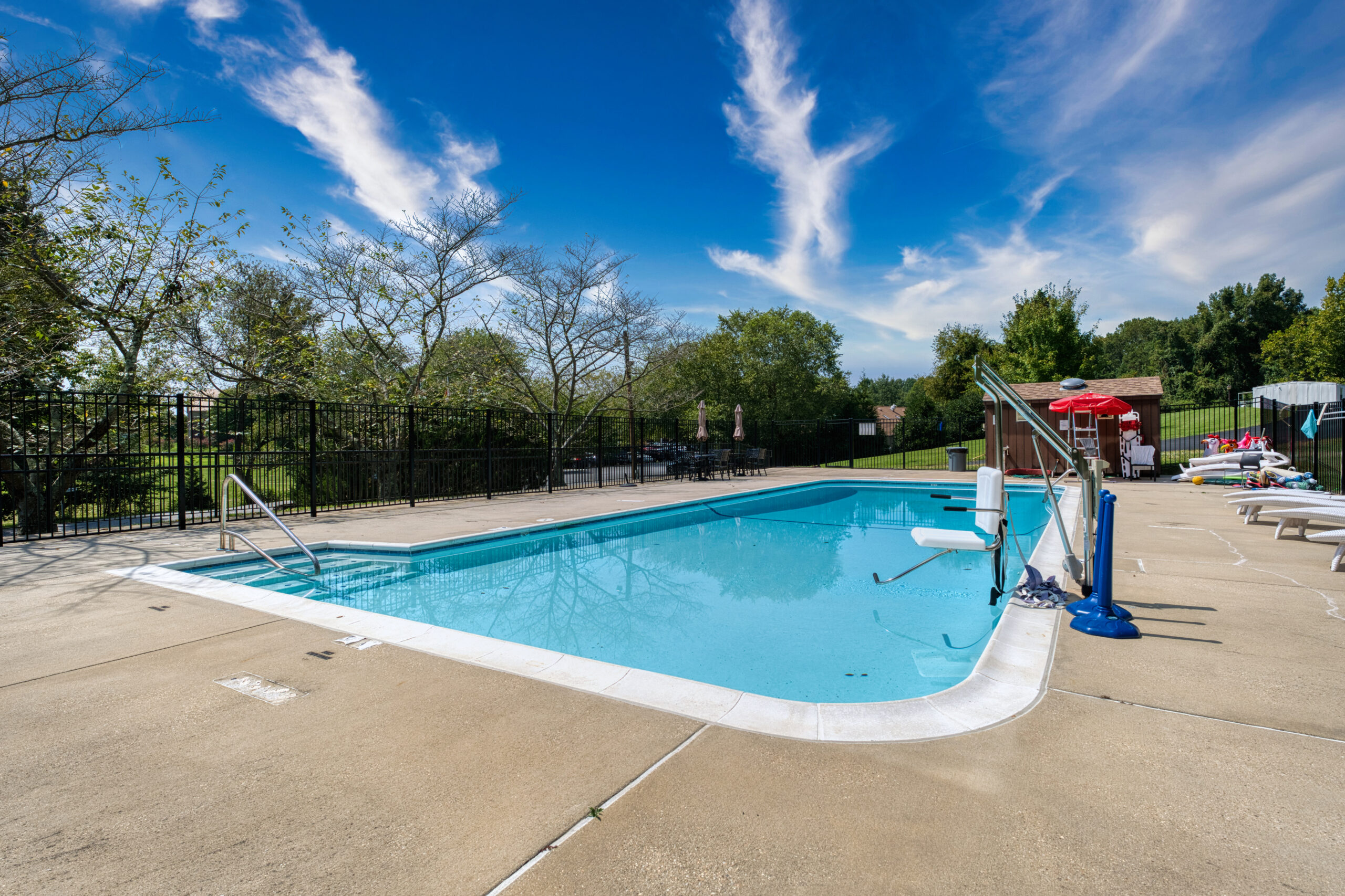 Outdoor swimming pool with lounge chairs and fenced area.