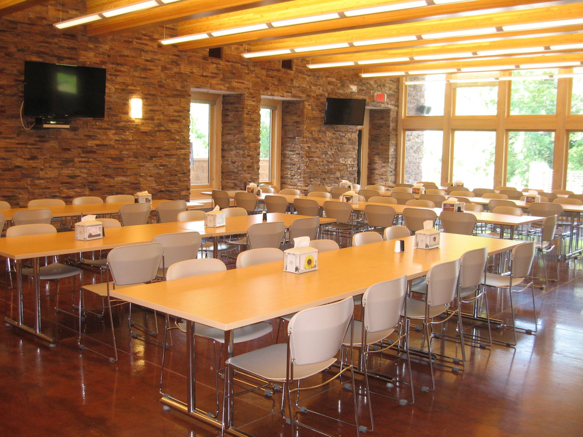 Bright dining hall with long wooden tables and mounted TVs