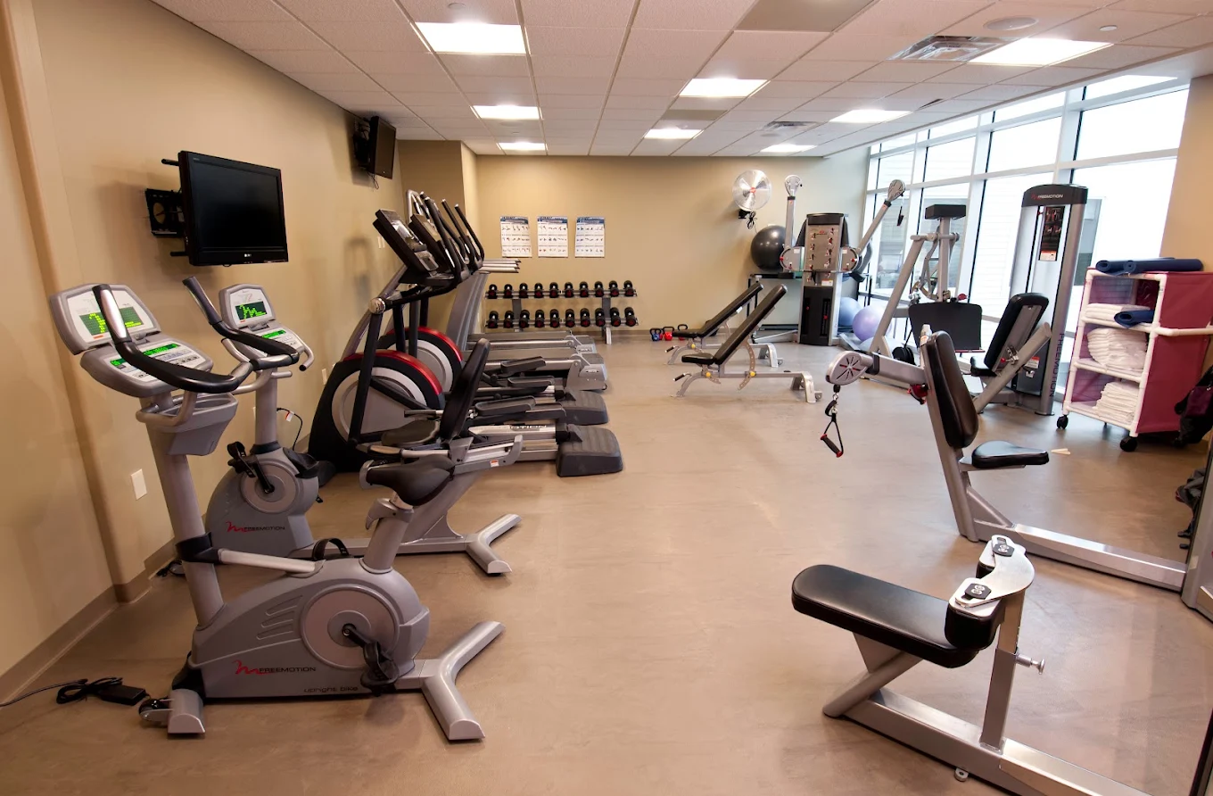 Fitness room with exercise bikes, strength equipment, weights, and large windows
