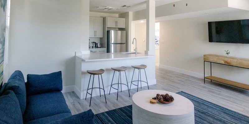 A modern living space featuring a comfortable blue couch, a sleek kitchen with barstools, and an inviting open layout with natural lighting.