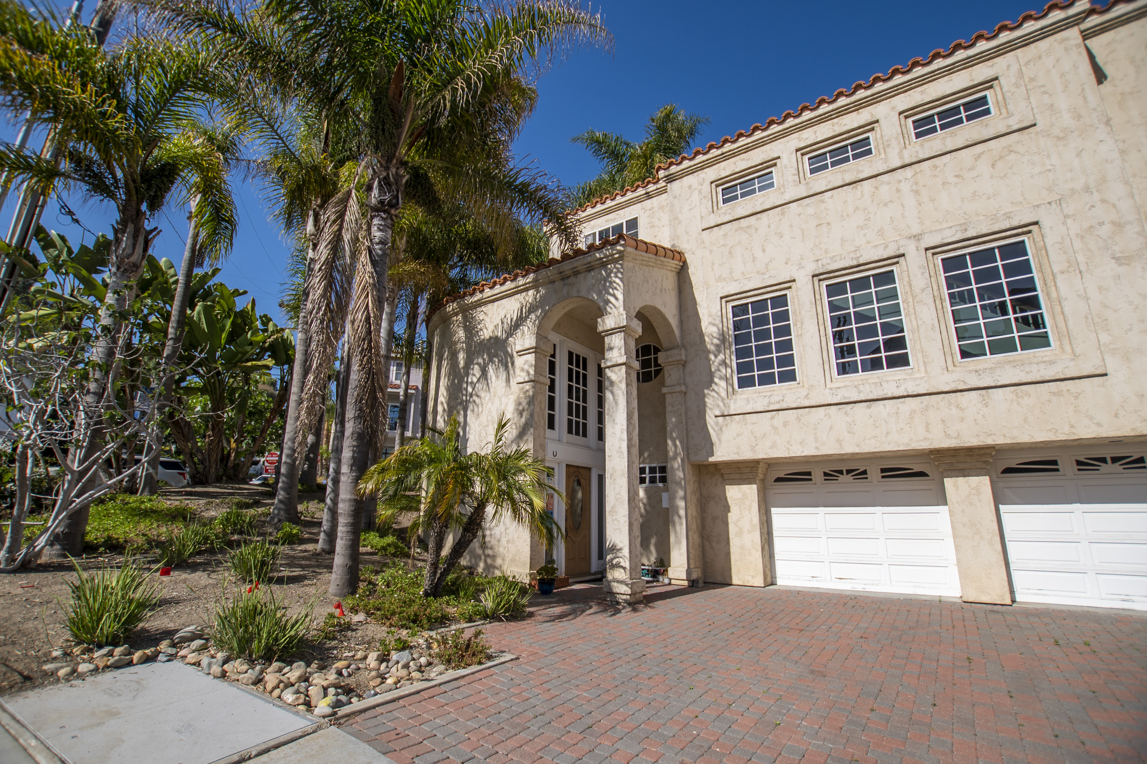 Stucco exterior with palm trees and a three-car garage