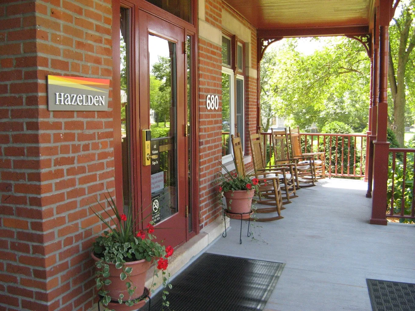 Covered brick porch at Hazelden with rocking chairs, potted flowers, and a tree-lined setting