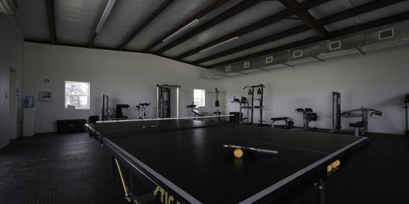 A spacious recreational room featuring a ping pong table and various exercise equipment, offering a mix of fun and fitness activities.