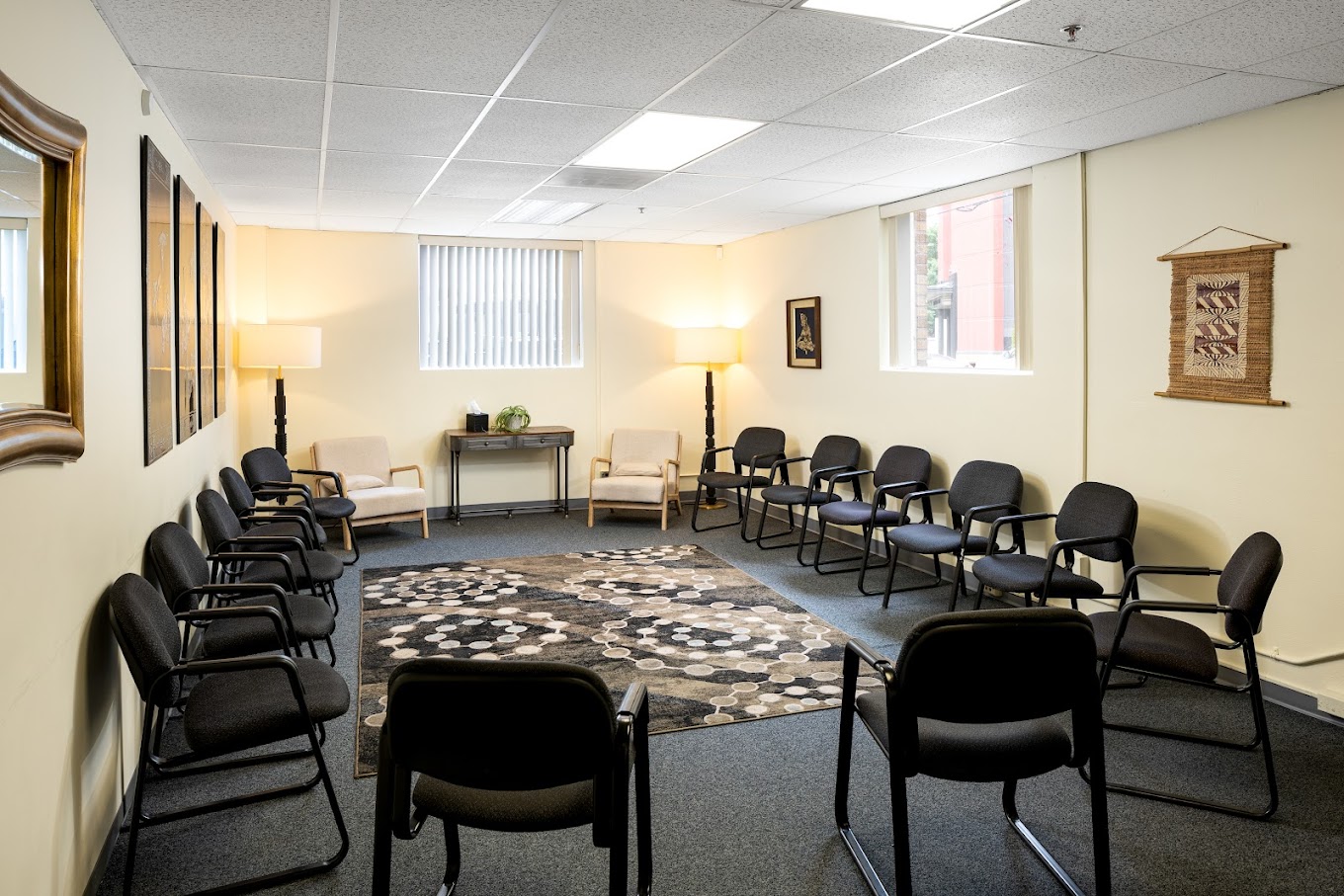 Group therapy room with black chairs and beige walls.