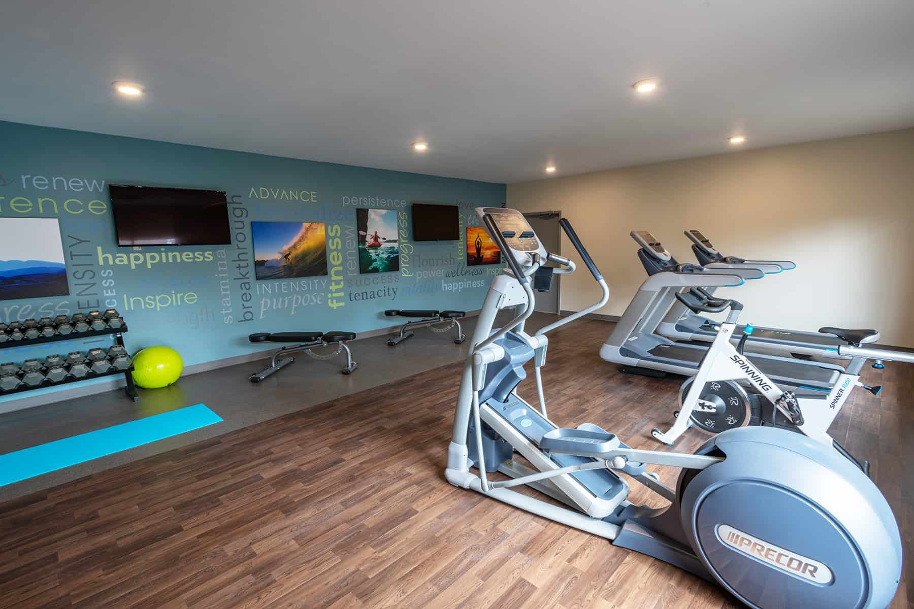 A modern gym with treadmills, weights, and motivational wall art.