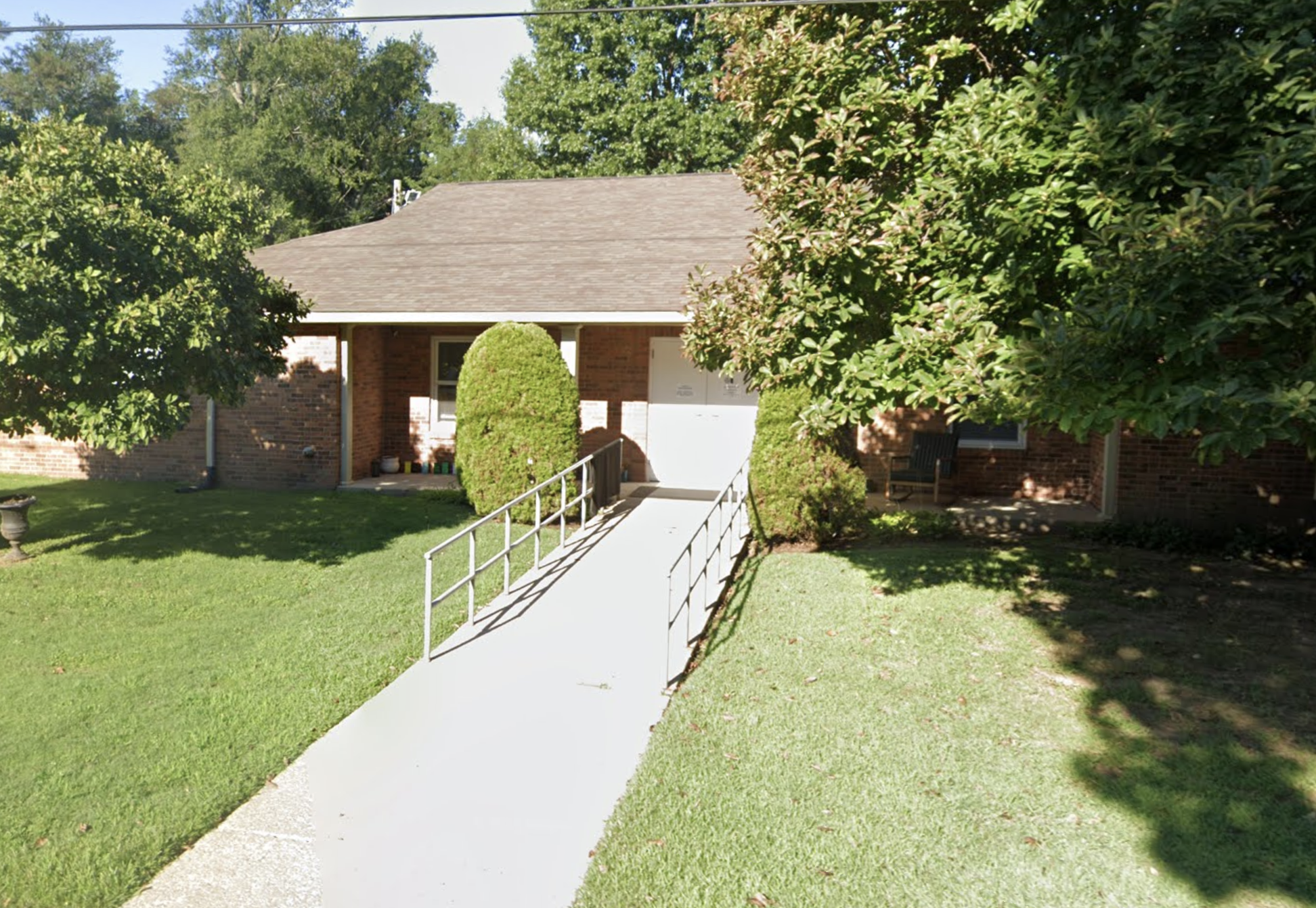 Brick building with entrance ramp, green lawn, and trees