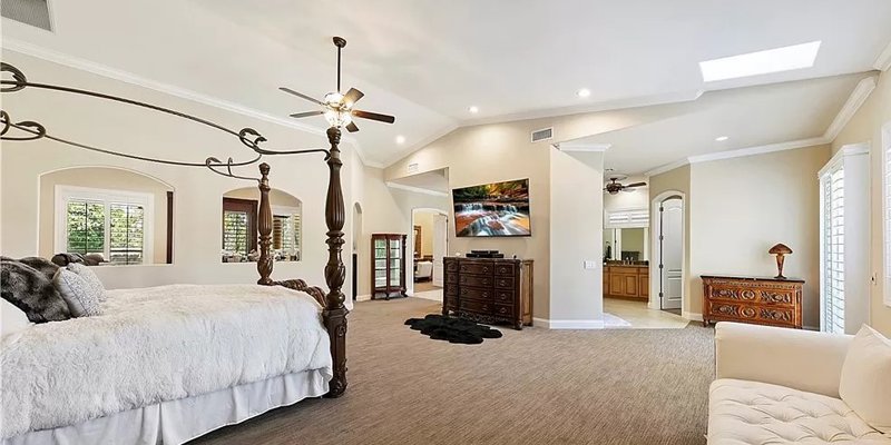 Elegant master bedroom featuring a spacious layout, a grand four-poster bed, plush carpeting, and soft natural light filtering through windows.